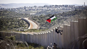<p> A Palestinian youth places a flag on the Israeli wall during a protest marking 9 years for the struggle against the wall in the West Bank village of Bilin, February 28, 2014.</p>